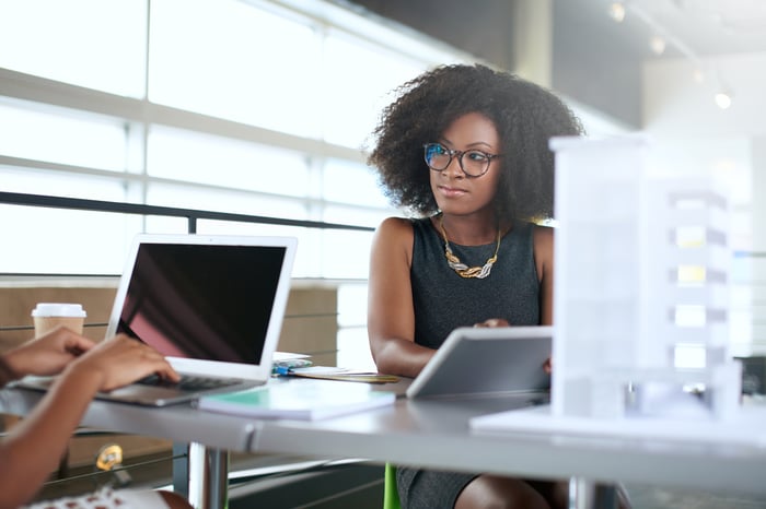 Woman in office working on computer and talking to colleague